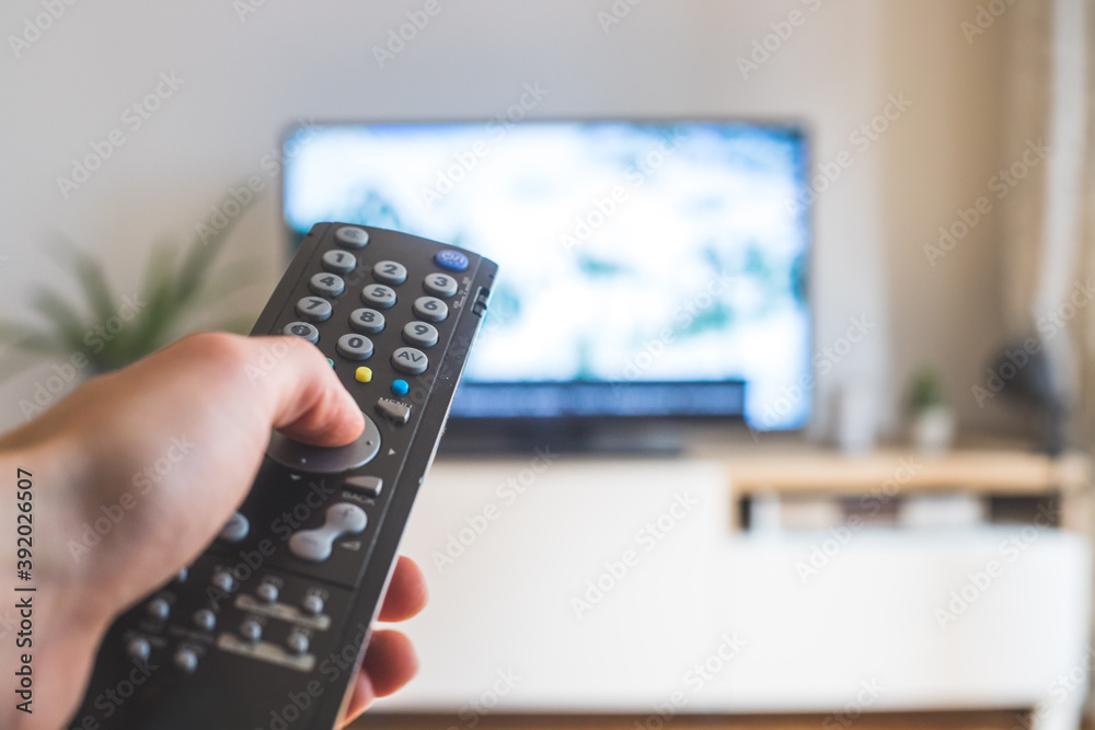 Male hand is holding TV remote control, streaming on a smart TV. Male hand is holding TV remote control, streaming on a smart TV.