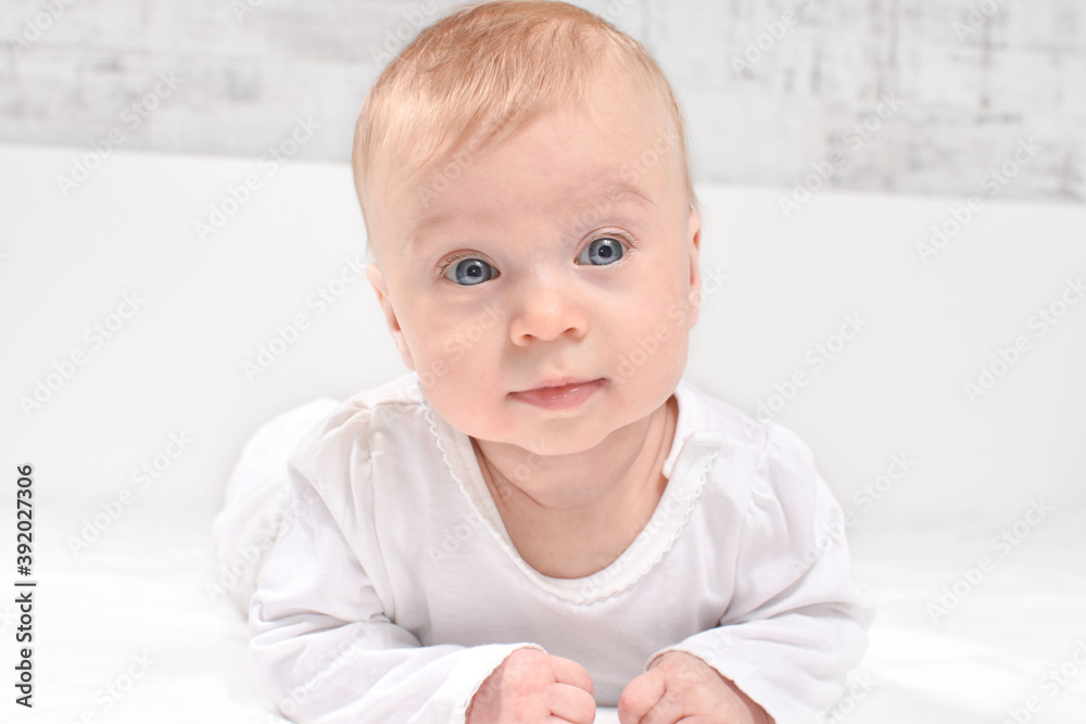 Adorable, caucasian baby girl or boy lying on stomach, on white blanket, looking at camera, on white background. Healthy skin. Baby care concept. Adorable, caucasian baby girl or boy lying on stomach, on white blanket, looking at camera, on white background. Healthy skin. Baby care concept.