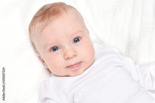 Portrait of Adorable, caucasian baby girl or boy lying on white blanket, looking at camera, on white background. Healthy skin. Baby care concept.