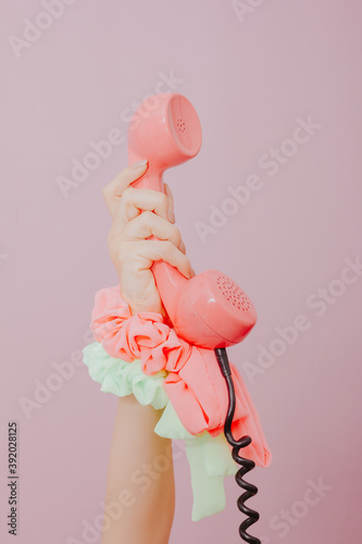 female hand holding an old pink phone on pink background.