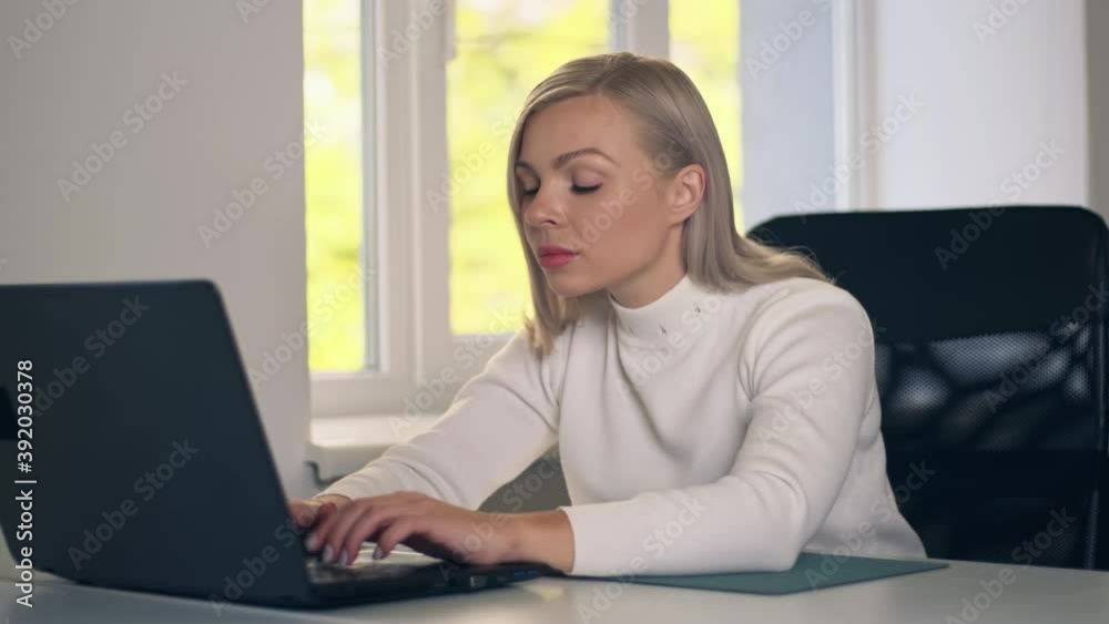 Confident businesswoman sitting at her desk and working on a laptop in home office. Stylish beautiful woman typing at laptop for job.. Confident businesswoman sitting at her desk and working on a laptop in home office. Stylish beautiful woman typing at laptop for job..