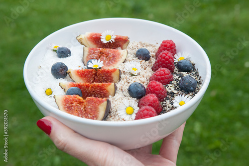 Bowl of sweet oatmeal with fresh fruit. Figue, blueberry, raspberry and decorative flowers