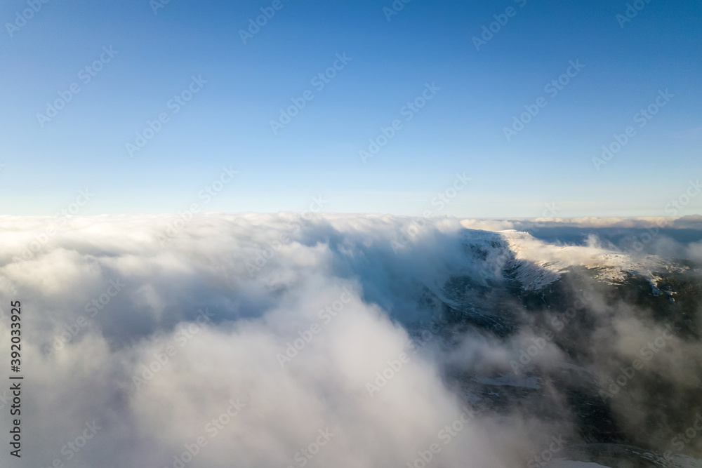 Aerial view from above of white puffy clouds covering snowy mountain tops in bright sunny day. Aerial view from above of white puffy clouds covering snowy mountain tops in bright sunny day.