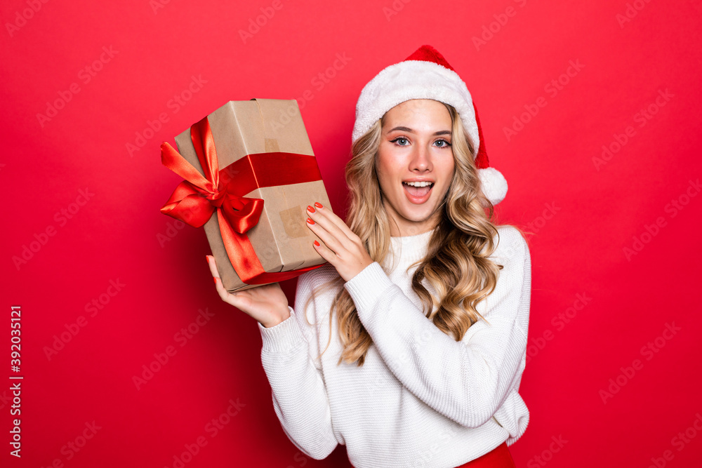 Φωτογραφία Beautiful young woman holding christmas gift wearing in santa hat isolated on re