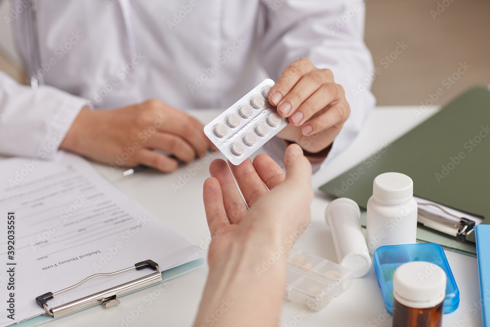 Fototapeta premium Close-up of doctor sitting at the table giving pills to her patient at hospital