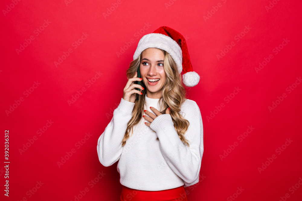 Happy cute woman in santa hat talking on cell phone over red background Happy cute woman in santa hat talking on cell phone over red background