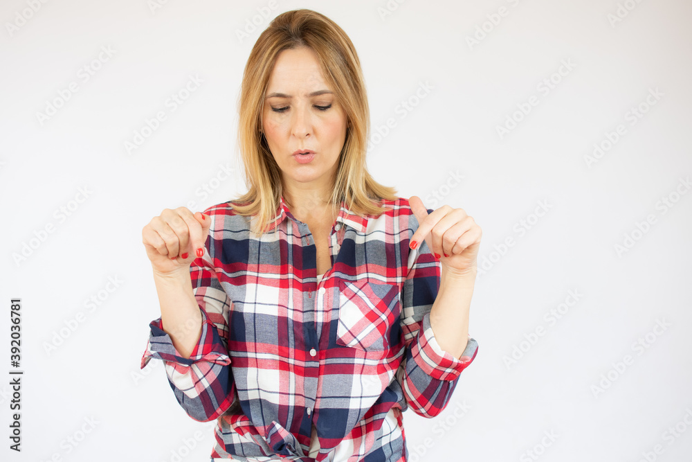 Young woman wearing plaid shirt over white background pointing down with fingers showing advertisement, surprised face and open mouth Young woman wearing plaid shirt over white background pointing down with fingers showing advertisement, surprised face and open mouth