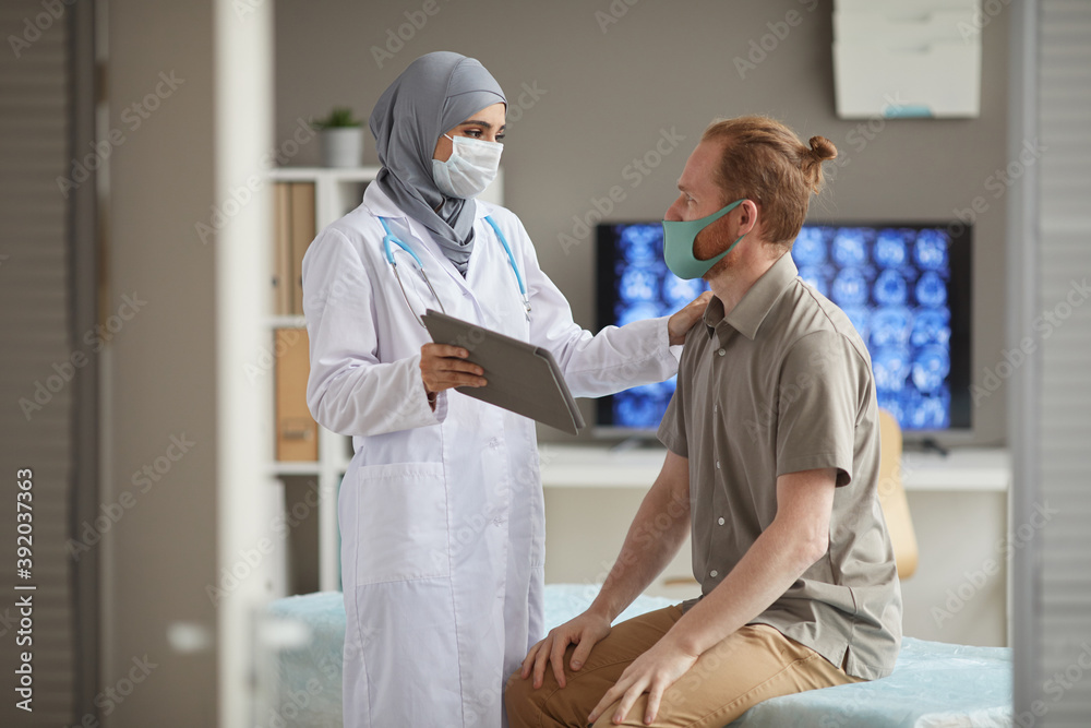 Obraz premium Female doctor in protective mask using digital tablet treating the patient at hospital