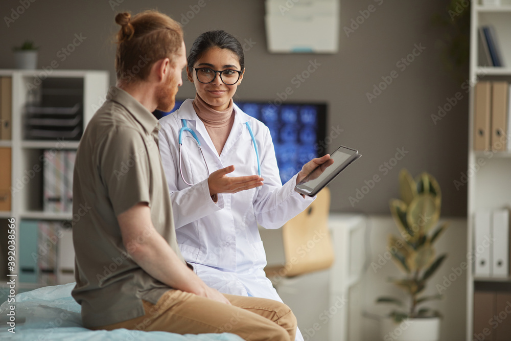 Young nurse in white coat showing medical recipe on digital tablet and talking to the patient during his visit at hospital Young nurse in white coat showing medical recipe on digital tablet and talking to the patient during his visit at hospital