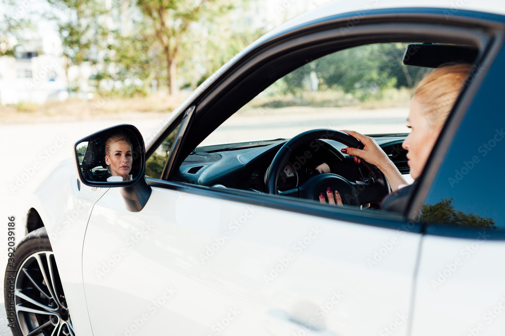 Beautiful female blonde driver behind the wheel of a white car