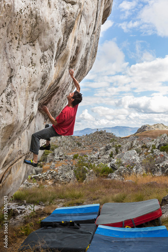 Athletic male climbs outside on a boulder in a grassy, rocky field photo