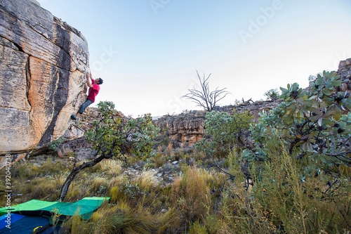 Athletic male climbs outside on a boulder above crash pads photo