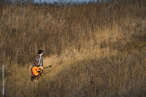 Country musician with acoustic guitar walks in grasses at a field photo