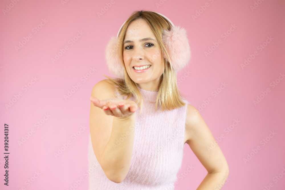 Portrait of a lovely young woman in pink earmuffs sending kiss isolated over pink background Portrait of a lovely young woman in pink earmuffs sending kiss isolated over pink background