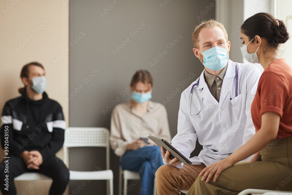 Obraz premium Male doctor using tablet pc and talking to woman at the corridor of hospital with other people in the background