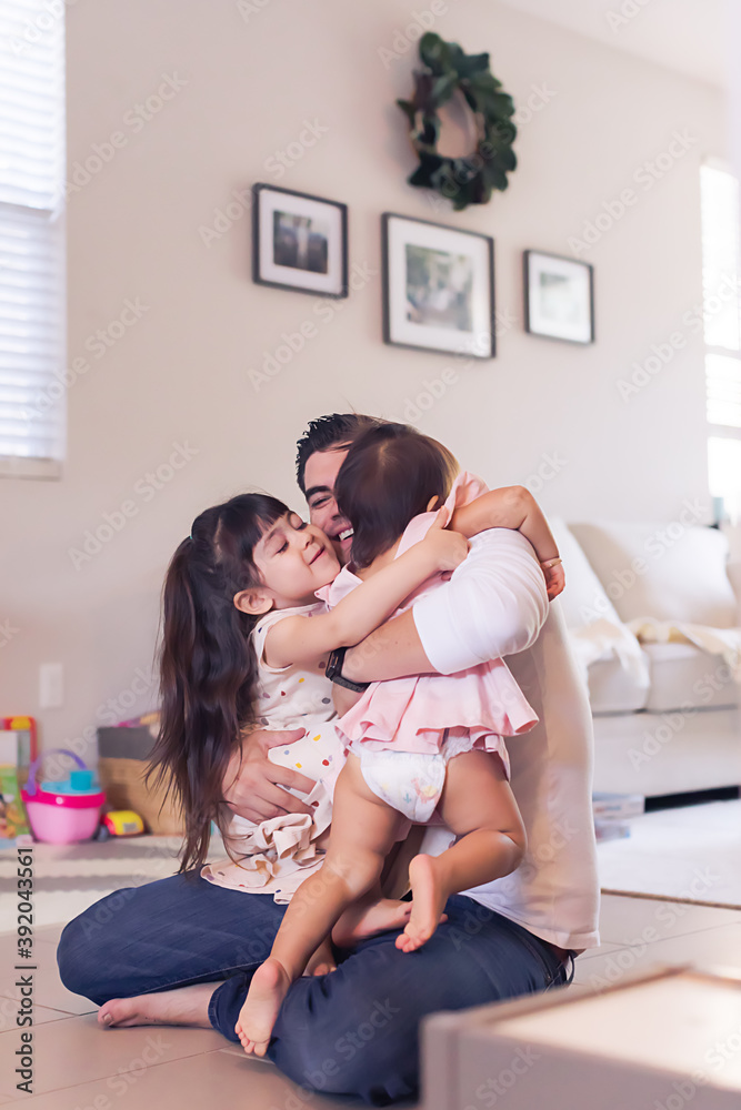 Dad sitting on the living room floor holding both daughters