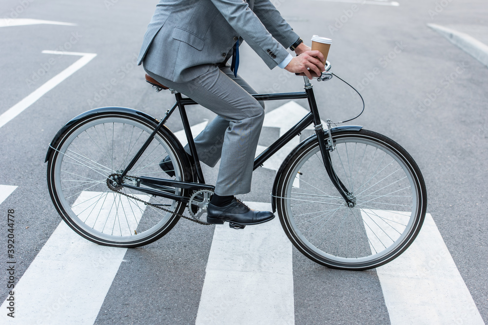 Cropped view of businessman holding takeaway coffee while cycling on crosswalk Cropped view of businessman holding takeaway coffee while cycling on crosswalk