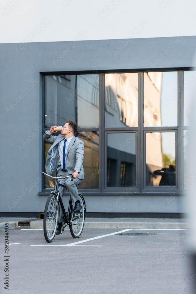 Young businessman drinking coffee to go while cycling near building