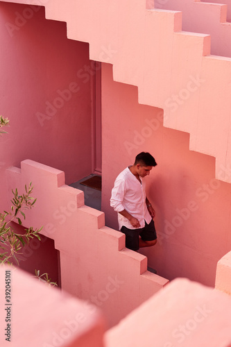 Young latin man goes down the stairs of a pink building