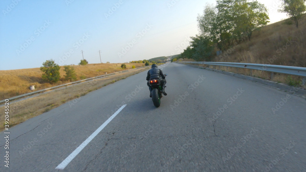 Aerial shot of man riding on modern sport motorbike at autumn highway. Motorcyclist racing his motorcycle on country road. Guy driving bike during trip. Concept of freedom and adventure. Above view