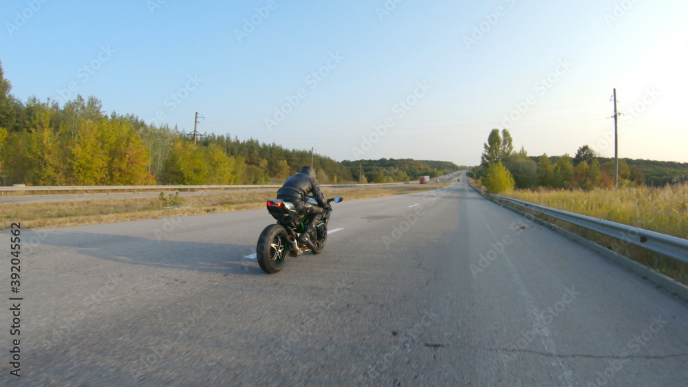 Biker riding on modern sport motorbike at highway during sunny autumn day. Motorcyclist racing his motorcycle on country road. Guy drive bike during trip. Concept of freedom and adventure. Aerial shot