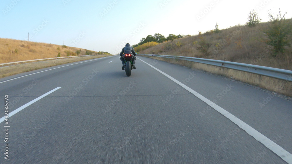 Follow to biker riding on modern sport motorbike at autumn highway. Motorcyclist racing his motorcycle on country road. Man driving bike during trip. Concept of freedom and adventure. Aerial shot Follow to biker riding on modern sport motorbike at autumn highway. Motorcyclist racing his motorcycle on country road. Man driving bike during trip. Concept of freedom and adventure. Aerial shot