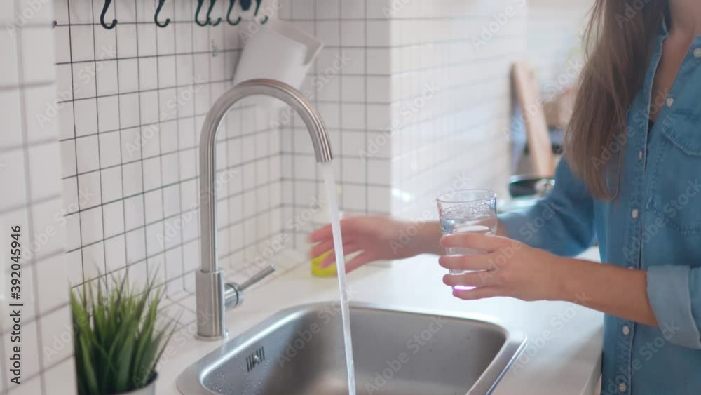 Woman pouring clean filtered water from the tap in glass for drinking at modern loft style kitchen