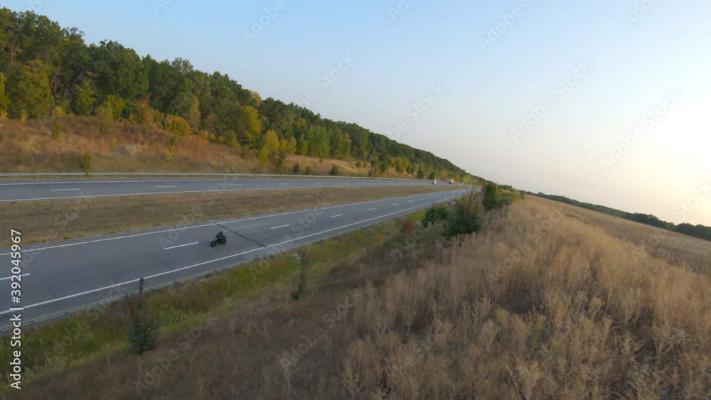 Aerial shot of motorcyclist riding on modern sport motorbike at autumn highway. Biker racing his motorcycle on country road. Guy driving bike during trip. Concept of freedom and adventure at journey Aerial shot of motorcyclist riding on modern sport motorbike at autumn highway. Biker racing his motorcycle on country road. Guy driving bike during trip. Concept of freedom and adventure at journey