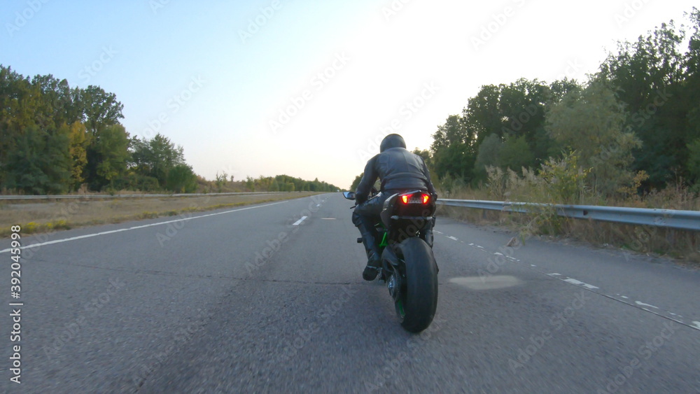 Camera moving around of biker riding on modern sport motorbike at highway. Motorcyclist racing his motorcycle on country road at sunset. Man driving bike during trip. Concept of freedom and adventure