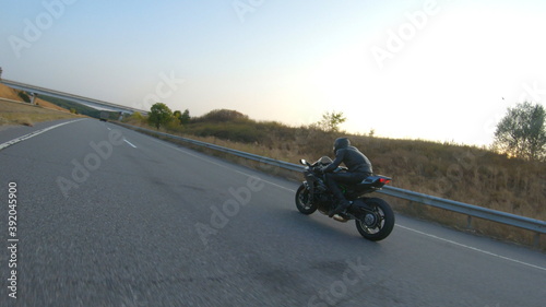 Man riding on modern sport motorbike on country road at sunny day. Motorcyclist racing his motorcycle at highway. Guy drive bike during trip. Concept of freedom and adventure at travel. Aerial shot