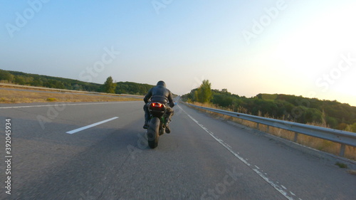 Biker is driving motorbike during road trip at autumn sunset time. Man ride fast on modern sport motorcycle at highway. Motorcyclist racing his bike on country road. Concept of adventure. Aerial shot © olehslepchenko