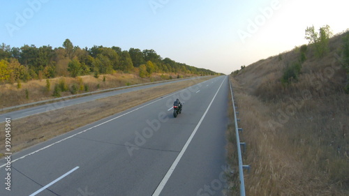 Aerial shot of motorcyclist riding on modern sport motorbike at autumn highway. Biker racing his motorcycle on country road. Guy driving bike during trip. Concept of freedom and adventure at journey