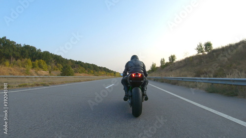 Biker is accelerating at motorcycle on empty country road. Man riding fast on modern sport motorbike at autumn highway. Guy driving bike during trip. Concept of freedom and adventure. Aerial shot