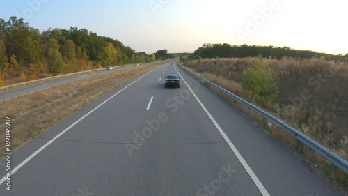 Aerial view of black car driving on countryside road. Automobile riding along highway during trip. Flying over auto moving along motorway. Concept of freedom and adventure at travel. Back view