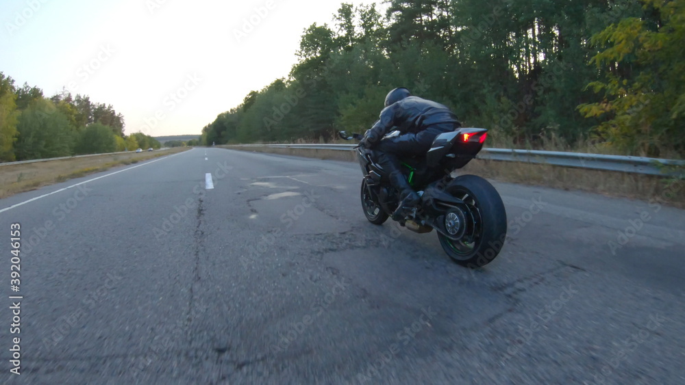 Aerial shot of motorcyclist riding on modern sport motorbike at autumn highway. Biker racing his motorcycle on country road. Guy driving bike during trip. Concept of freedom and adventure at journey