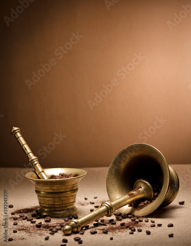 bronze mortar and pestle, with natural coffee beans and ground powder, on raffia cloth and brown background
