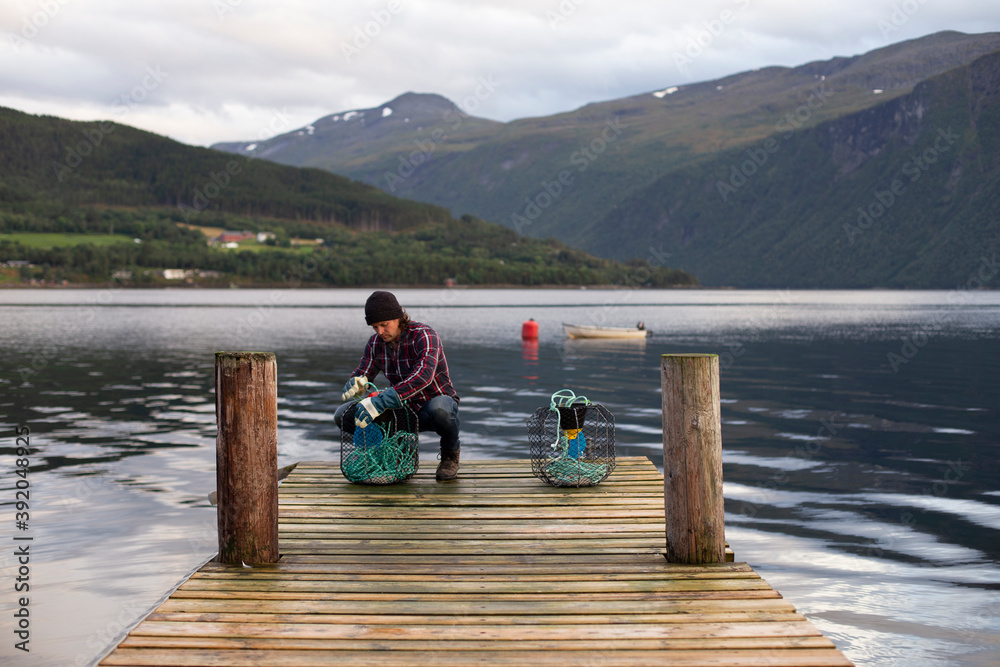 A Norwegian working on some crab pots on a dock by the fjord A Norwegian working on some crab pots on a dock by the fjord