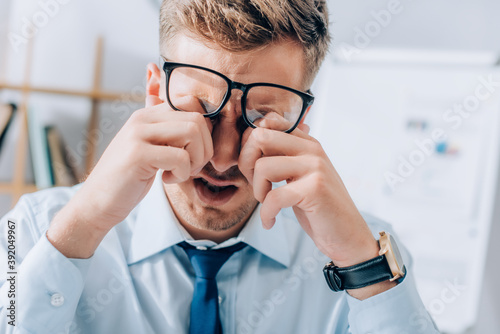 Exhausted businessman rubbing eyes while working in office