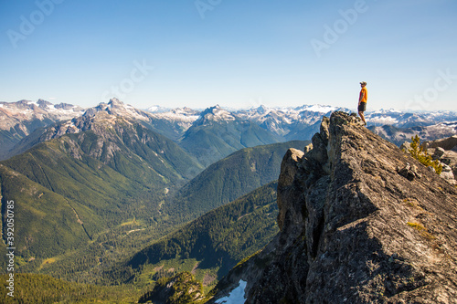 Man on mountain summit looking out at view of forest and peaks. photo