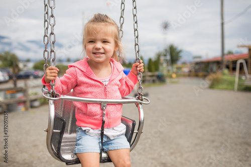 Cute young girl sitting on metal swing outside. photo