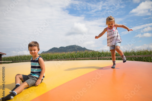 Brother and sister enjoying time outdoors, jumping on trampoline.