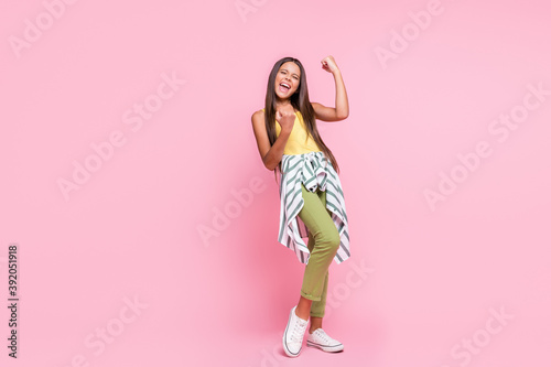 Full size photo of triumphant girl celebrate goal raise fists closed eyes wear green pants isolated on pink color background