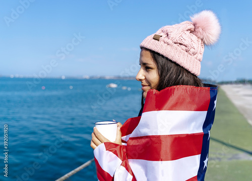 Beautiful young woman standing wrapped in the American flag with a cup photo