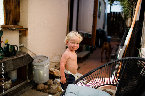 Two Year Old Smiling for Camera While Standing on Side of House photo