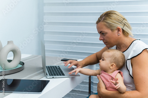 MOM TELEWORKING AND WITH HER BABY IN ARMS