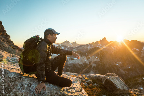 Backpacker sits on mountain summit enjoying view of sunset. photo