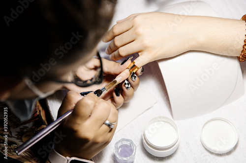 From above stylist applying polish on tip of nail of crop customer photo