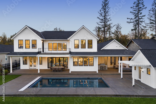 Modern farmhouse luxury home exterior with in ground pool at twilight