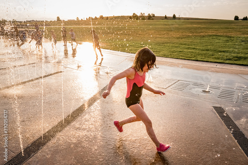 young girl in bathing suit runs through splash pad of squirting water