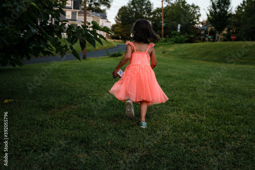 girl in orange dress holding toy truck running in grass photo